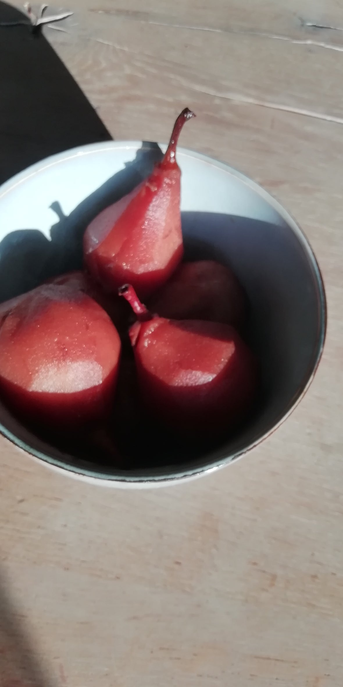 een schaaltje mooie rode stoofperen. de zon schijnt op de peren en het schaaltje. het schaaltje staat op een houten tafel met noesten