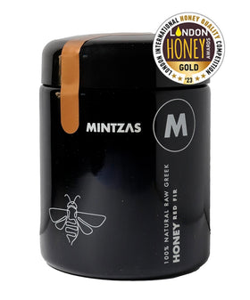 Een zwarte cilinder vormige pot met een bijpassende zwarte deksel. De pot is vergrendeld met een gouden lint. Daarnaast is de zwarte port met zilvere letters bedrukt en is een BIJ getekent doormiddel van een doorlopende lijn.